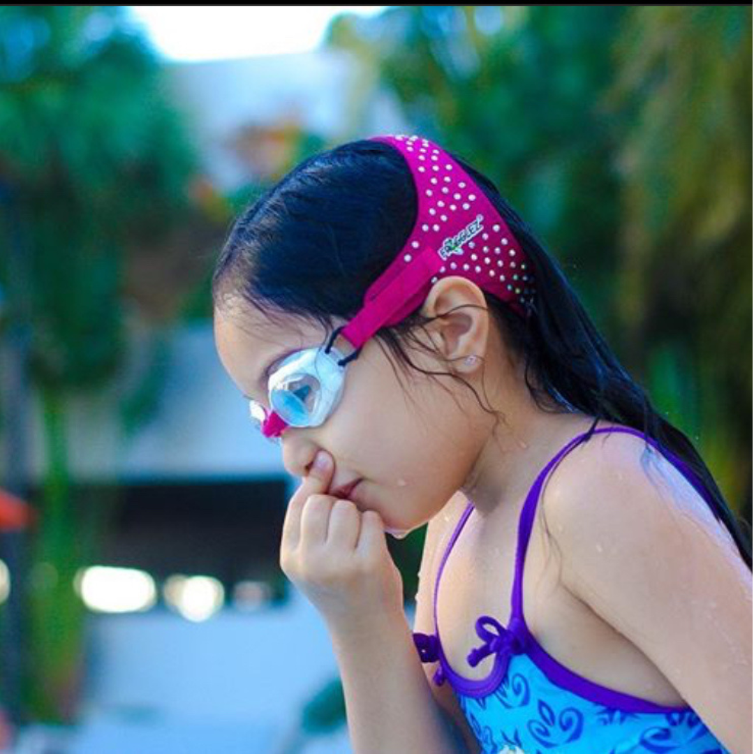 Girl holding her nose closed before diving into the water while wearing pink glitz Frogglez Goggles.