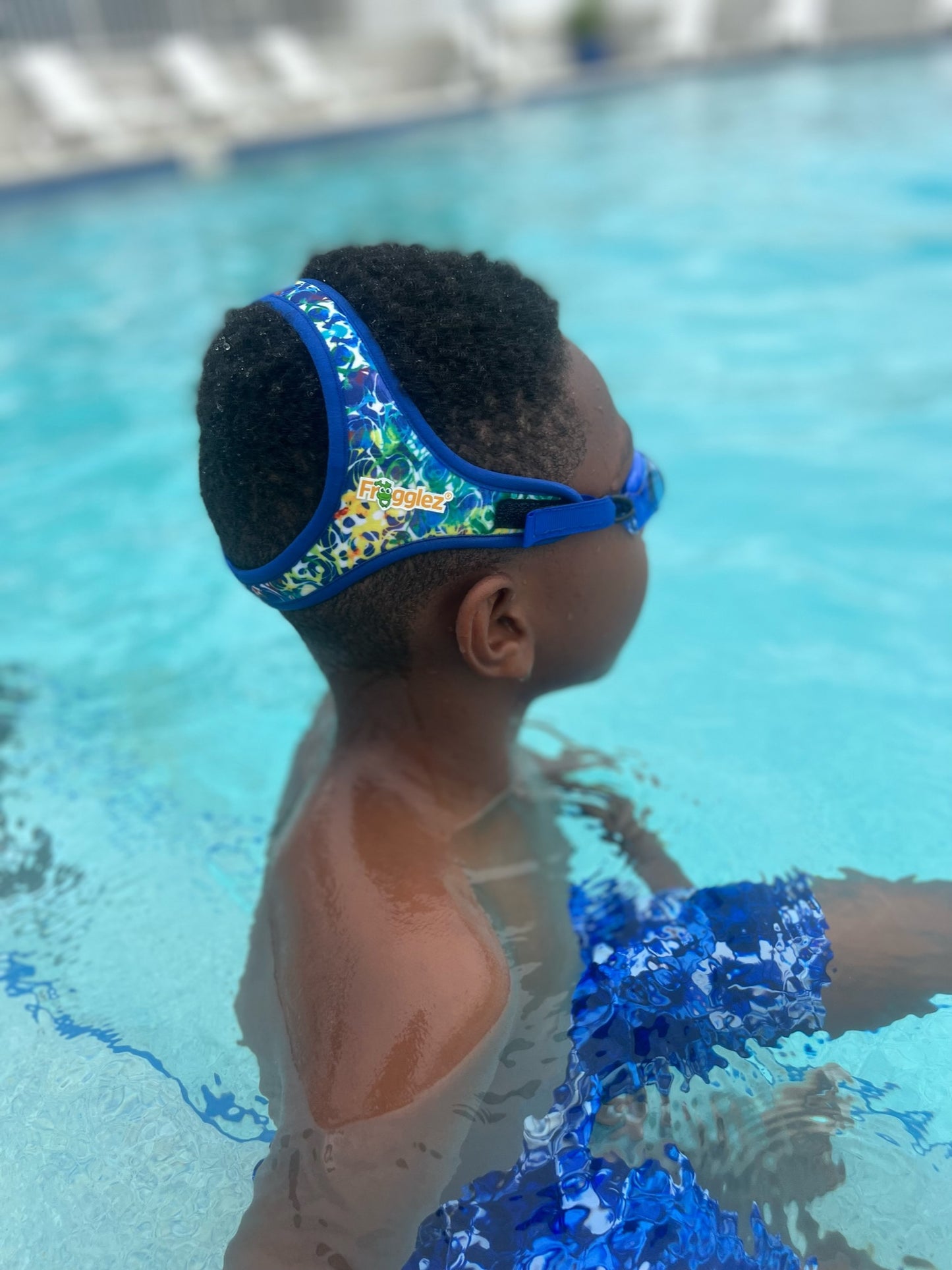 Young boy sitting in a pool looking away from the camera. Showing off the Frogglez Blue Waves pattern